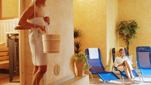 A spa area with a woman in a towel holding a bucket, two lounge chairs, and a potted plant. - Apartment Dahoam (Forstau)