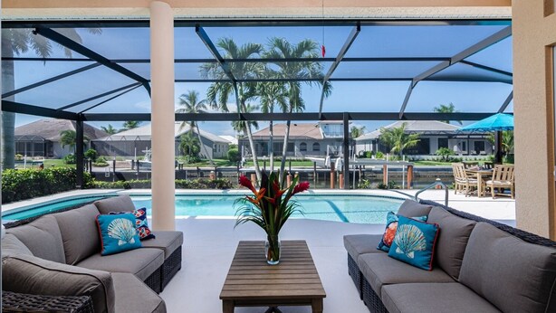 A covered outdoor area with a pool, two sofas, a table, and a ceiling fan.