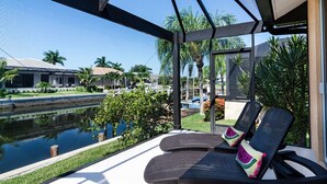 A covered outdoor seating area with two lounge chairs and a small pool.