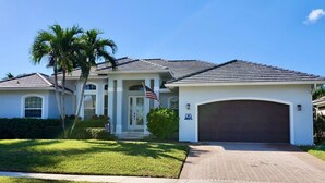 A single-story house with a front garage, a well-maintained lawn, and a palm tree.