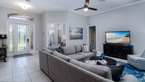 A modern living room with a sectional sofa, a flat-screen TV, and a ceiling fan.