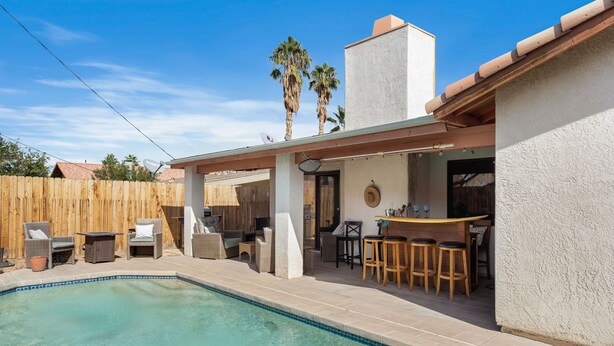 A backyard with a swimming pool, outdoor furniture, and a bar area.