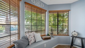 A room with a built-in bench, a clock on a small table, and a window with blinds.