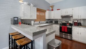 A modern kitchen with white cabinets, granite countertops, and stainless steel appliances. There are three bar stools with woven seats.