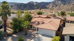 A residential area with houses featuring red-tiled roofs, surrounded by palm trees and mountains in the background.