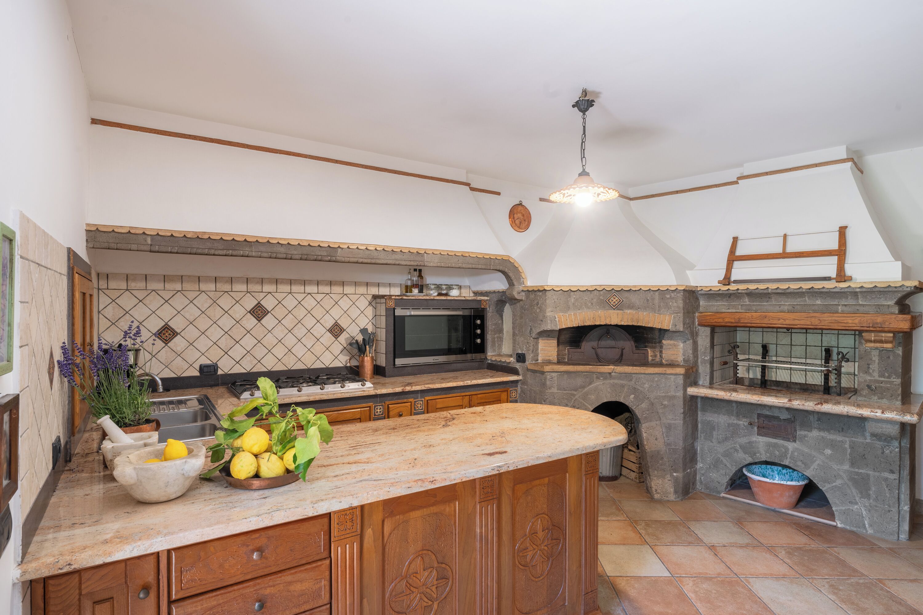 A kitchen with a stone oven, a microwave, and a wooden island with a bowl of lemons and herbs.