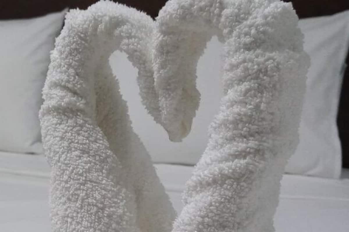 A bed with white linens and two white towels arranged in a heart shape.