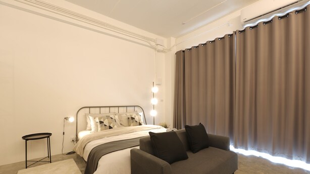 A modern bedroom with a bed, a sofa, a small table, and a large window with curtains. - Loft Series (Krabi)