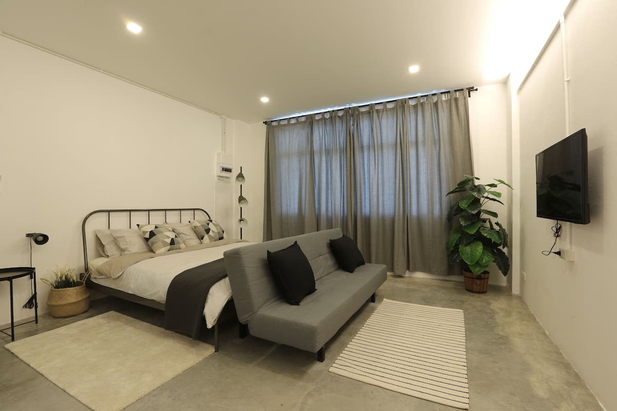 Un dormitorio moderno con cama, sofá y televisor montado en la pared.