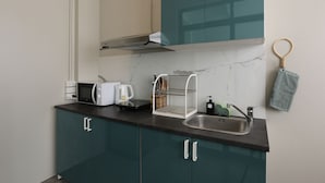 A kitchen with teal cabinets, a stainless steel sink, a microwave, a toaster, and a dish rack. - Loft Series (Krabi)