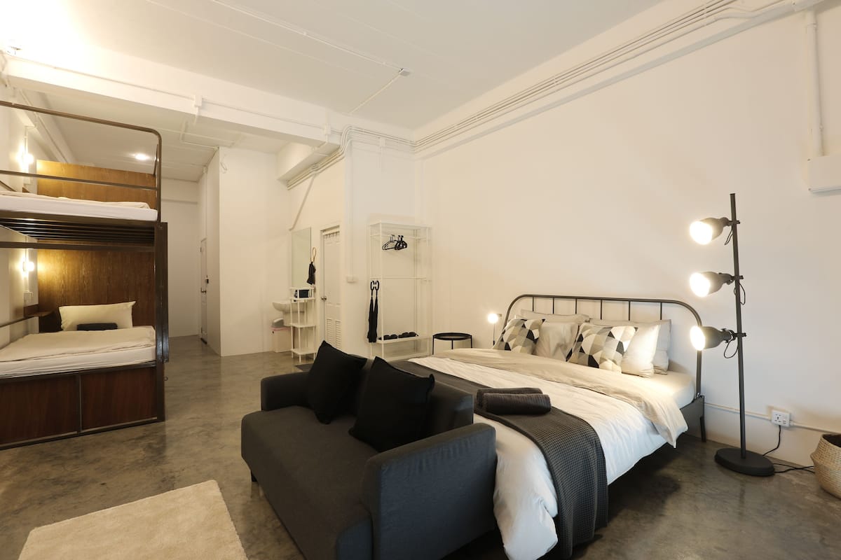 Un dormitorio moderno con una cama alta, un sofá, una mesita de noche y una lámpara de pie.