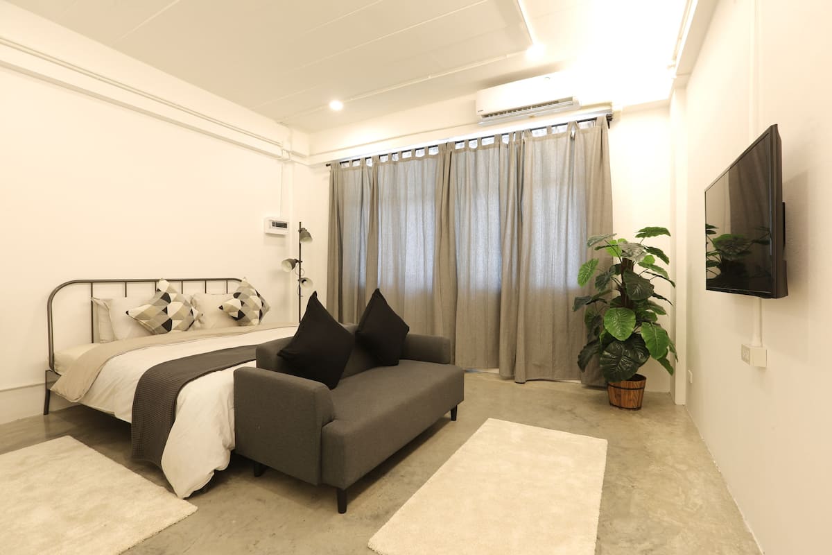 Un dormitorio moderno con cama, sofá, televisor y un ventanal con cortinas.