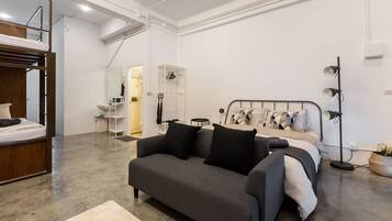 Una habitación moderna y luminosa con una cama litera, un sofá gris, una cama grande con muchas almohadas y una lámpara de pie.