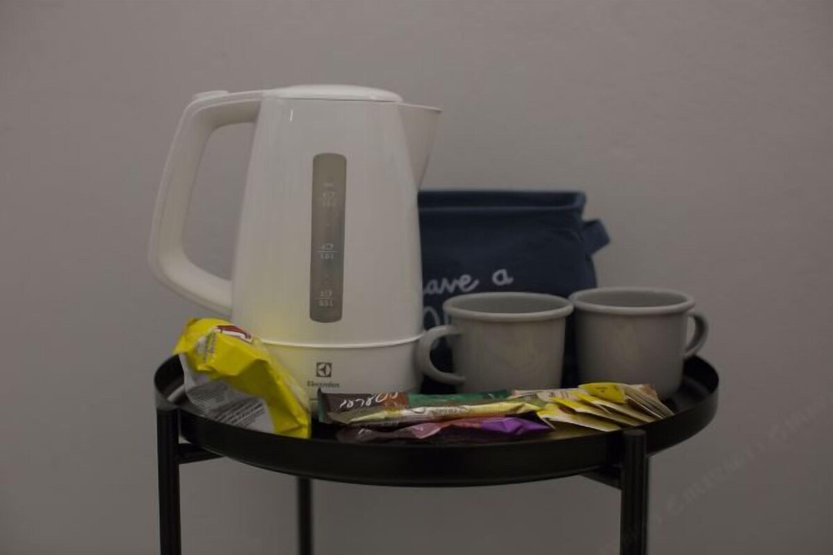 A black tray with a white electric kettle, two white cups, and a blue bag with a slogan.