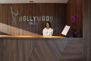 A reception desk with a wooden panel design, a logo reading "Hollywood De Luxe," and a potted orchid. - Hollywood De Luxe Hotel (Krasnodar)