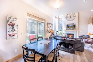Un salón amplio con chimenea, un comedor con una mesa grande y sillas, y un televisor montado en la pared.