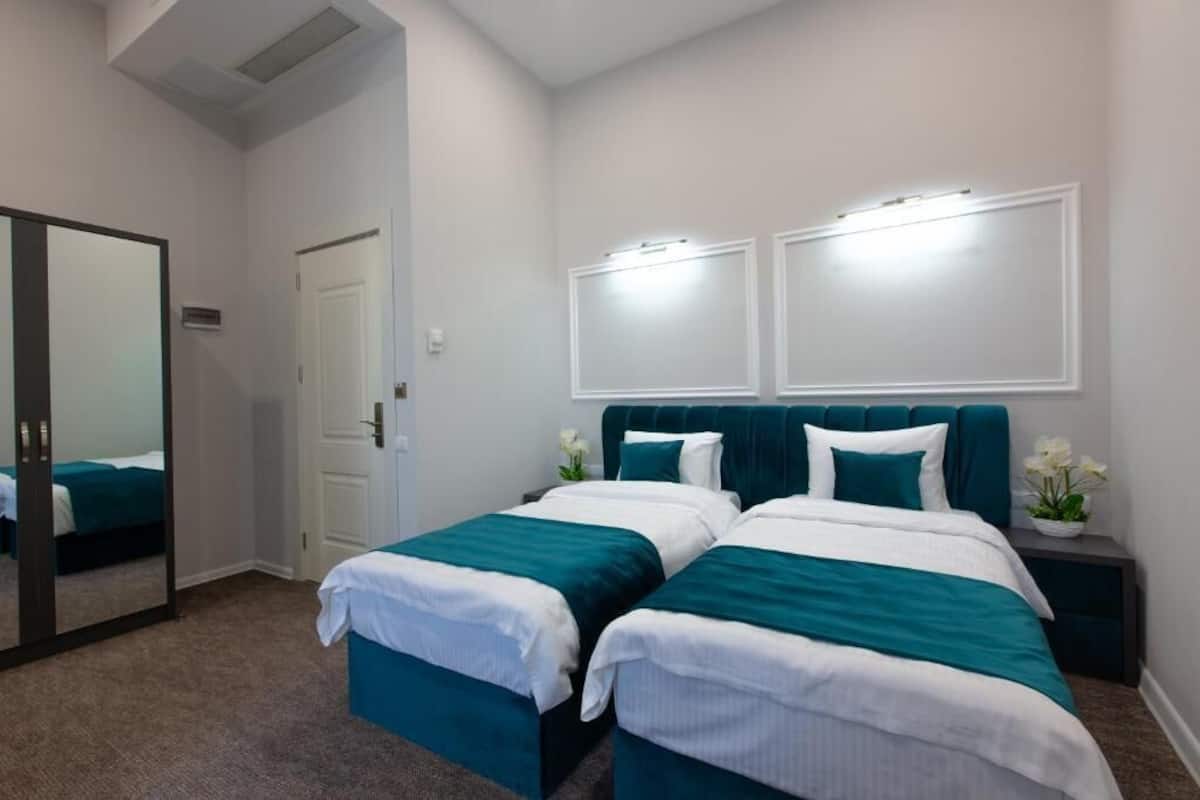 Quarto de hotel com duas camas de solteiro, um espelho grande, uma porta e uma mesa de cabeceira com uma planta.