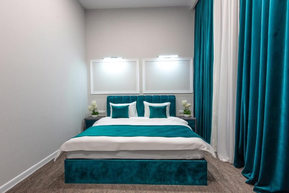 Une chambre à coucher bien rangée, avec un lit, des tables de chevet et une grande fenêtre avec des rideaux.
