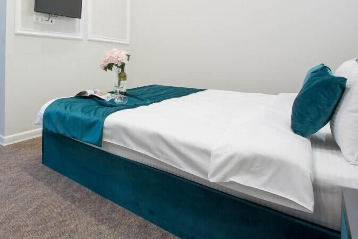 Quarto com cama, televisão de tela plana na parede e um vaso com flores na mesa de cabeceira.