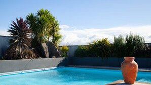 A swimming pool with clear blue water, surrounded by various plants and a large terracotta pot. - Rural South Wairarapa Home - Views,Swimming & Spa Pool (Taumata Island)