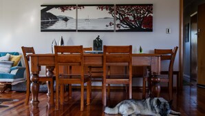 A dining area with a wooden table and chairs, a painting on the wall, and a dog lying on the floor. - Rural South Wairarapa Home - Views,Swimming & Spa Pool (Taumata Island)