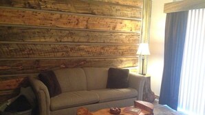 Ein Wohnzimmer mit Holzwand, einer Couch, einem Couchtisch, einer Lampe und einem Fenster mit Vorhängen.