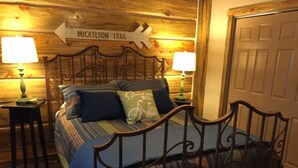 Ein Zimmer mit Holzboden, einem Bett, zwei Nachttischen und einer Tür. Ein Schild an der Wand zeigt "Mickelson Trail".