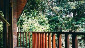 Une terrasse en bois, un mur en briques et une vue sur une végétation luxuriante.