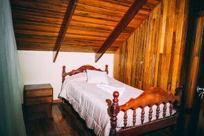 Un dormitorio con techo de madera, estructura de cama de madera, mesita de noche y panel de pared de madera.