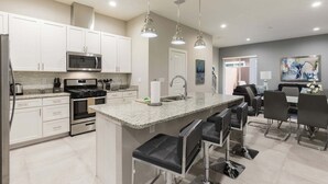 A modern kitchen with white cabinets, stainless steel appliances, and a central island with bar stools. - ★Amazing Hidden Gem | Min ➡️ Disney | ❤ 139 (Kissimmee)