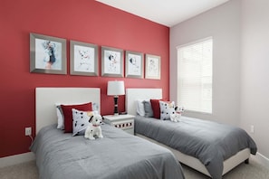 Quarto com duas camas, parede vermelha e quadros acima das camas.