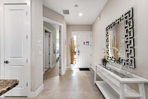 Un pasillo con puertas blancas, una consola blanca y un florero, y un espejo decorativo.