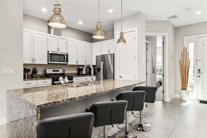 Cozinha moderna com bancadas de granito, eletrodomésticos de aço inoxidável e banquetas.