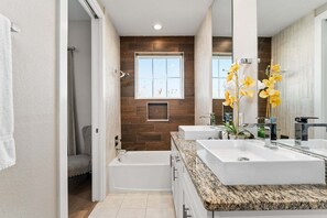 Un baño moderno con bañera, dos lavamanos, un espejo grande y una ventana.
