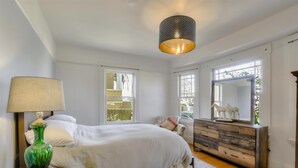 Een slaapkamer met een bed, dressoir, lamp en grote ramen.
