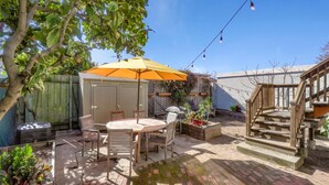 Een achtertuin met een patio, een ronde tafel, stoelen en een gele parasol.