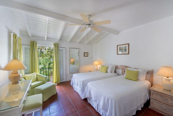 A bedroom with two beds, a ceiling fan, a balcony with curtains, and a desk with a lamp.