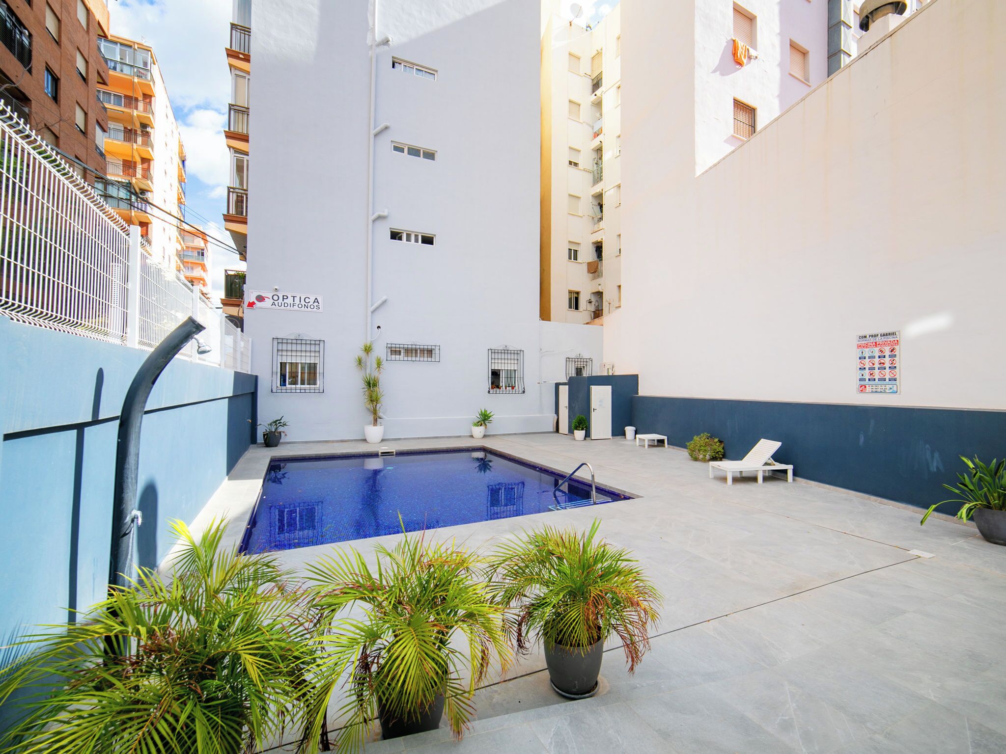 A swimming pool with lounge chairs and potted plants in an urban setting.