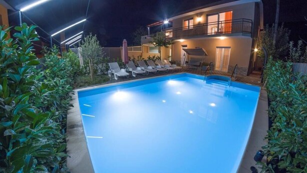 Ein Schwimmbad mit Liegestühlen, umgeben von Grünpflanzen, und ein Gebäude mit Balkon im Hintergrund.