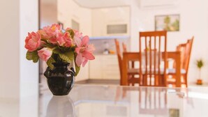 Ein Essbereich mit Tisch und Stühlen, eine Vase mit rosa Blumen und eine Küche im Hintergrund.