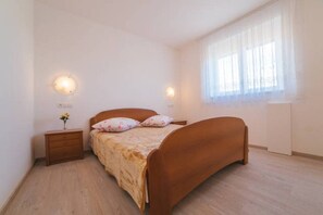 Une chambre à coucher avec un lit en bois, deux tables de chevet, une petite table et une fenêtre ornée de rideaux légers.
