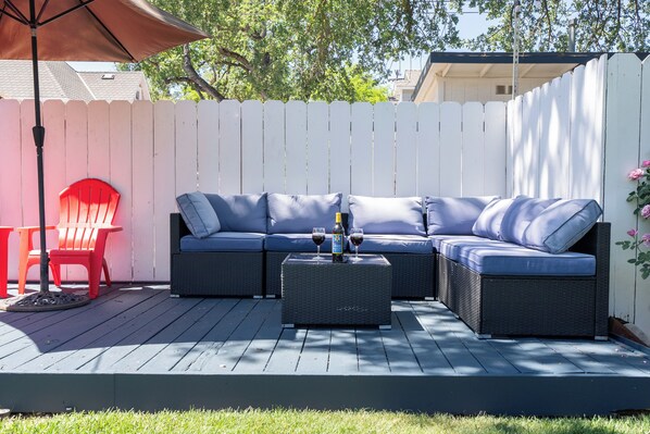 A deck with a sectional sofa, a small table, and a red chair. - Victorian Charm + BBQ Yard | Paso Robles Wine Country | Vacations on Vine (Paso Robles)