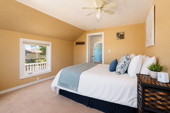 A bedroom with a bed, a ceiling fan, a window, and a door leading to another room.
