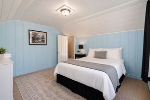 A bedroom with a bed, a nightstand, a lamp, a framed picture, and a door leading to another room. - Victorian Charm + BBQ Yard | Paso Robles Wine Country | Vacations on Vine (Paso Robles)