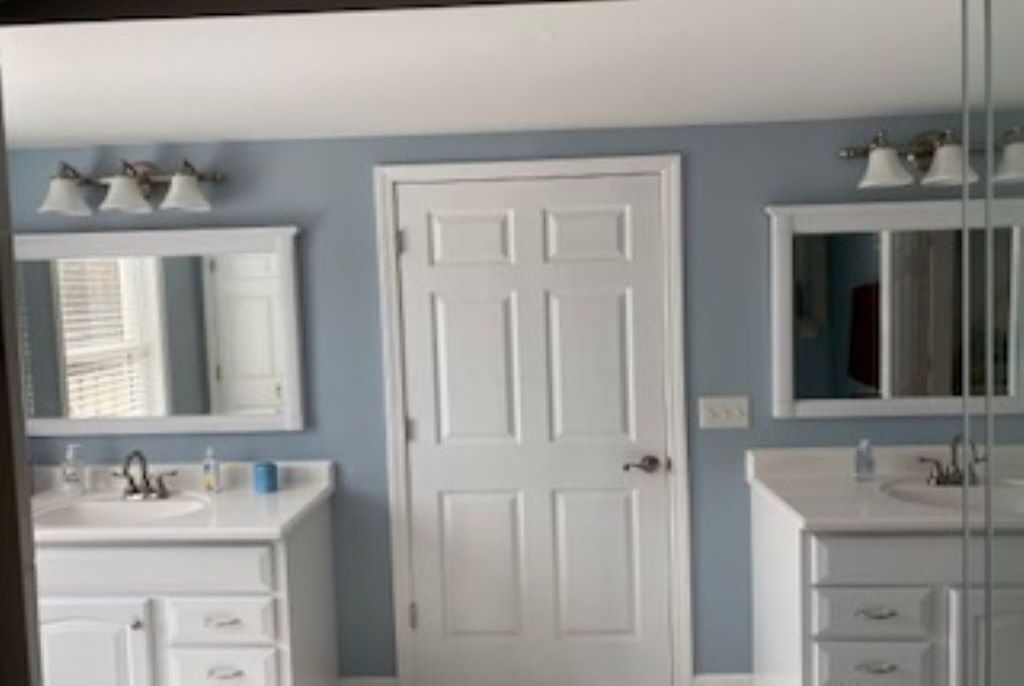 A bathroom with two sinks, a white door, and a mirror above each sink.