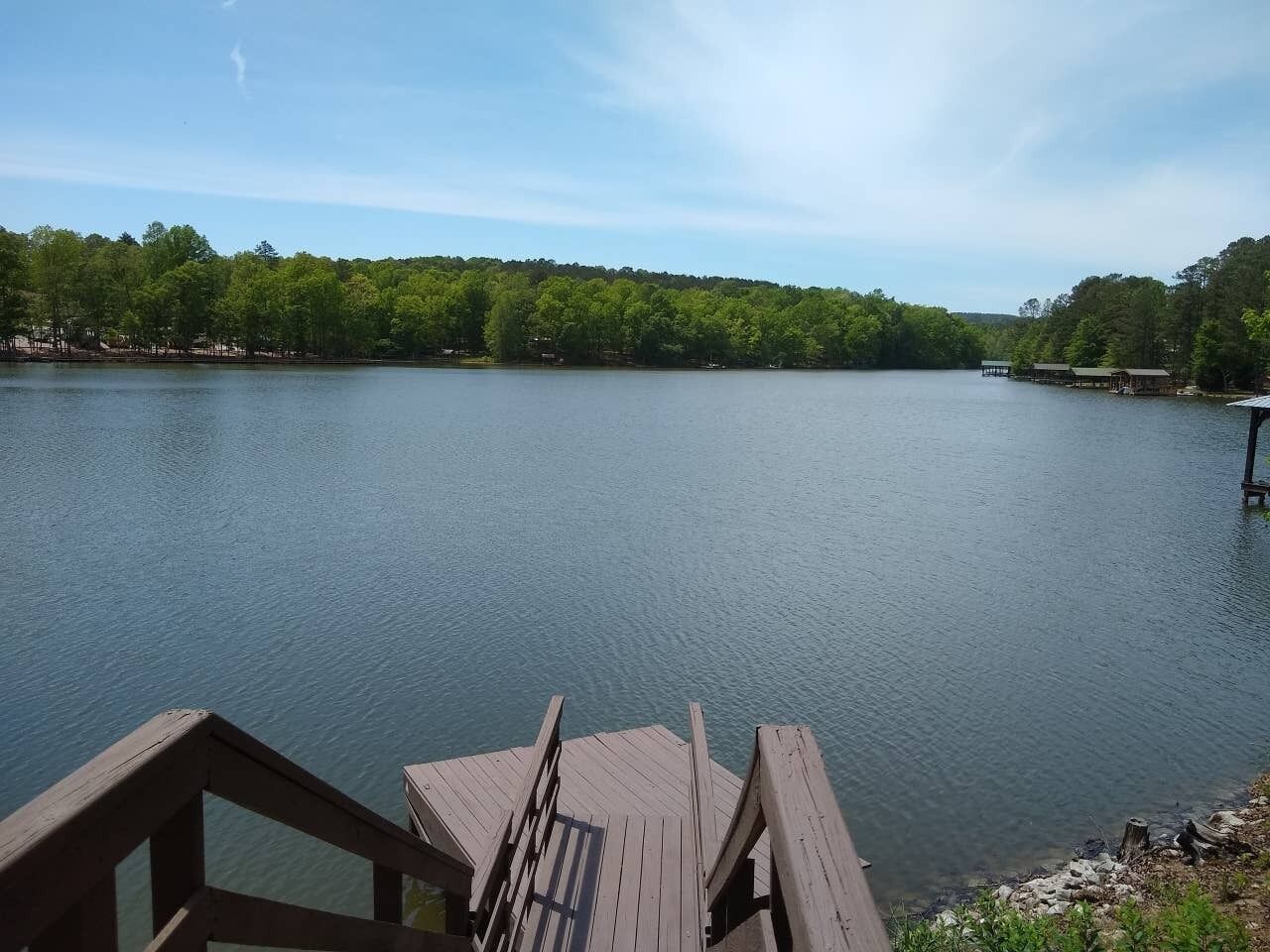 Une jetée en bois s’étendant sur un lac paisible, avec une rive boisée en arrière-plan.