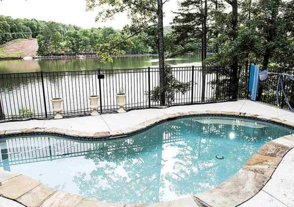 A swimming pool with a curved edge, surrounded by a stone deck and a metal fence.