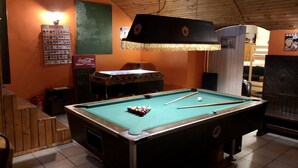 A pool table with balls, a foosball table, and a Coca-Cola refrigerator in a room with orange walls and wooden ceiling. - Whole basement former pub 4 stag do (VIII. kerület)