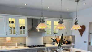 A modern kitchen with white cabinetry, a central island with bar stools, pendant lighting, and a heart-shaped wall decoration.