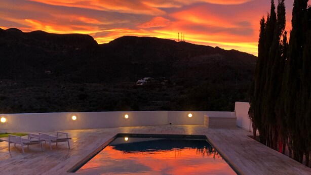 A rooftop pool with a view of a sunset over a mountainous landscape.